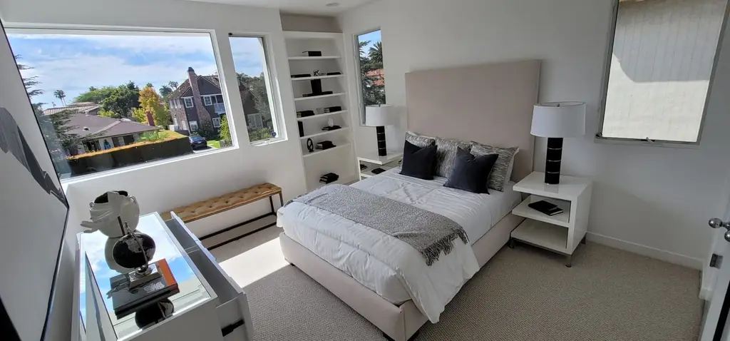 A made bed and tidy bedroom with a wide window looking out over the hills