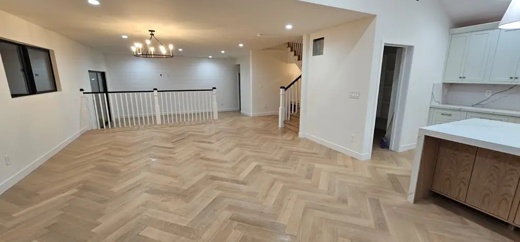 An empty open hall with a herringbone wood floor and a white stair rail