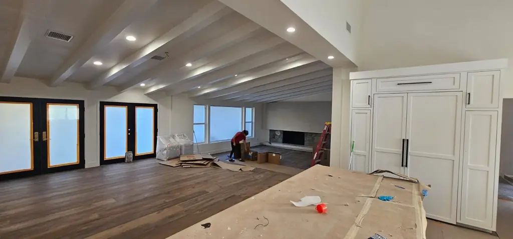 A large renovated room with beamed ceiling and floor protection still down, mid-clean