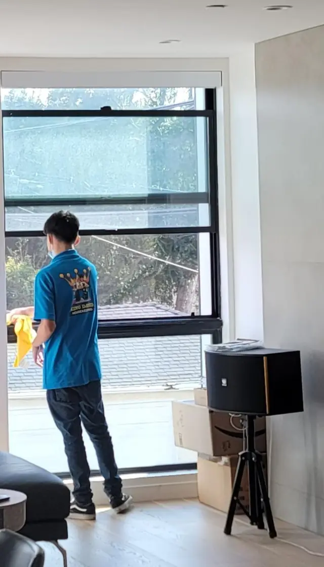A crew member in a blue King David shirt wiping a tall window